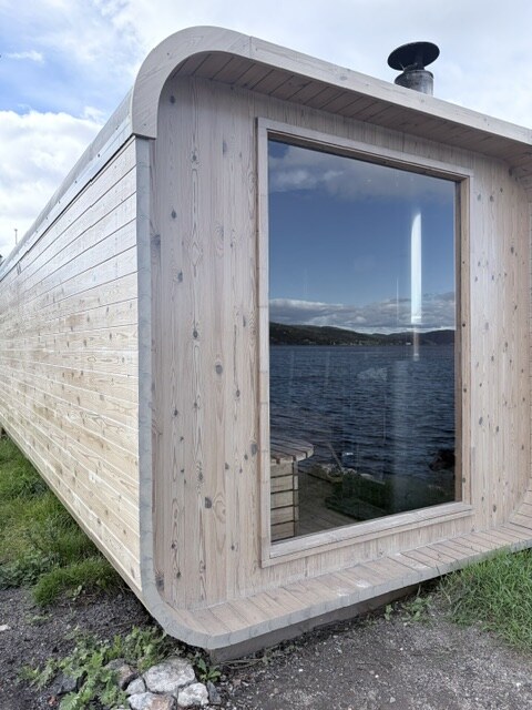 Utsiden av Brevik Badstue med sjøen speilet i vinduet